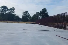 Thumbnail for Large concrete slab with a tall metal fence along one side and trees in the background under a cloudy sky