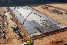 Thumbnail for Aerial view of a large concrete slab foundation being poured at a construction site with multiple cement mixers.