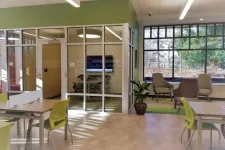Thumbnail for Modern office space with glass meeting room, green chairs, large window, and natural light filled room.