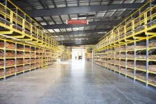 Thumbnail for Spacious warehouse with yellow industrial shelving stocked with wooden planks under a metal roof with bright lighting.