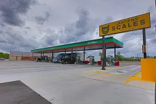 Thumbnail for Truck stop with multiple fuel pumps under canopy and a large certified scales sign on a cloudy day