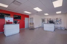Thumbnail for Spacious, modern service area with two white counters, red accent wall, and product displays under fluorescent lighting