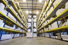 Thumbnail for Large warehouse aisle with tall blue and yellow racks filled with stacked cardboard boxes and packages.