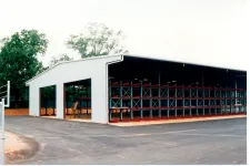 Thumbnail for Large open warehouse with metal shelving units and paved driveway surrounded by trees on a clear day