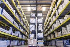 Thumbnail for Interior of a large warehouse with tall shelves stocked with boxes and packages on a concrete floor.