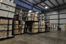 Thumbnail for Warehouse interior with large metal racks storing flat wooden panels and frames under industrial lighting.