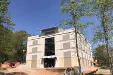 Thumbnail for Newly constructed beige commercial building surrounded by trees under a clear blue sky.