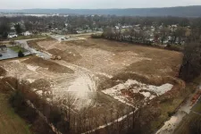 Thumbnail for Cleared and leveled construction site with earthmoving equipment near residential area under cloudy sky