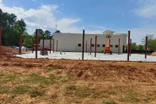Thumbnail for Construction site with steel beams installed on concrete foundation near a building under a blue sky.
