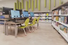 Thumbnail for Library computer station with multiple monitors and green chairs beside bookshelves filled with books.