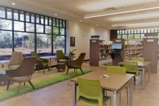 Thumbnail for Modern library reading area with large windows, wooden tables, green chairs, and bookshelves under bright lighting.