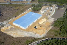 Thumbnail for Aerial view of a large warehouse under construction surrounded by cleared land and forest with a nearby pond.