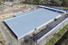 Thumbnail for Aerial view of a large metal-roofed warehouse under construction with surrounding construction equipment and materials.