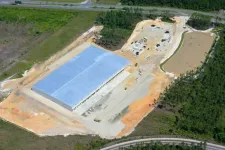 Thumbnail for Aerial view of a large warehouse under construction surrounded by cleared land and forested areas.