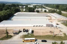 Thumbnail for Aerial view of large industrial warehouses under construction with vehicles on adjacent road under clear sky