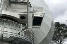 Thumbnail for Large white radar dome structure with metal platform railing and trees in the background under cloudy sky