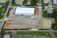 Thumbnail for Aerial view of industrial warehouse with adjacent construction site and retention pond in a commercial area.
