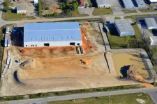 Thumbnail for Aerial view of a construction site with a large warehouse, dirt roads, and a murky pond in an industrial area.