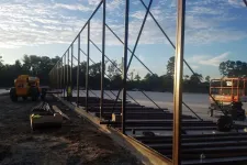 Thumbnail for Steel framework under construction at a large outdoor site during early morning with construction equipment present
