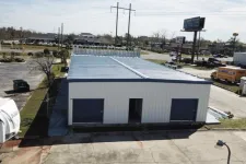 Thumbnail for A white metal warehouse building with two large garage doors and an open entrance under a clear sky.