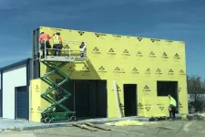 Thumbnail for Construction workers install yellow DensGlass sheathing on a commercial building under clear blue sky.
