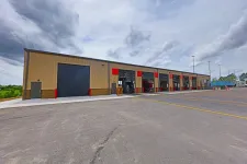 Thumbnail for Wide view of a large industrial building with multiple open garage bays and a paved parking area under cloudy sky
