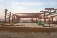 Thumbnail for Steel frame structure under construction with a green boom lift and concrete foundation at dusk.