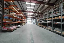 Thumbnail for Interior view of a large warehouse with metal racks holding wood and building materials under a steel roof.
