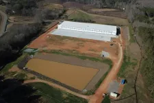 Thumbnail for Aerial view of a large construction site with a white warehouse building near a muddy water retention pond.