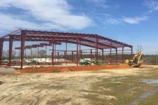 Thumbnail for Steel frame structure under construction on a clear day with construction equipment and muddy ground in the foreground