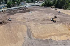 Thumbnail for Aerial view of a large dirt construction site with machinery and trucks working on land clearing near a residential area