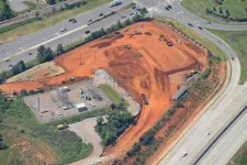 Thumbnail for Aerial view of a construction site with red soil, heavy machinery, and adjacent highways with traffic.