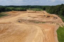 Thumbnail for Large construction site with dirt roads, heavy machinery, and forested background under partly cloudy sky