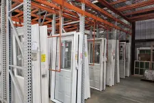Thumbnail for Rows of white doors with windows displayed on orange and gray metal racks inside a warehouse.
