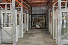 Thumbnail for Warehouse aisle with white doors and windows stored on metal racks under an orange ceiling grid