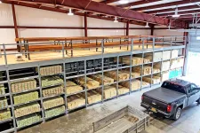 Thumbnail for Warehouse interior with stacked lumber on metal racks and a black pickup truck beside a wooden trailer under a metal roof