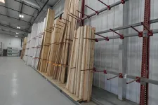 Thumbnail for Stacks of wooden planks stored vertically on red metal racks inside a warehouse with high ceilings.