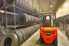 Thumbnail for Red Doosan forklift in a warehouse aisle surrounded by shelves stacked with black tires