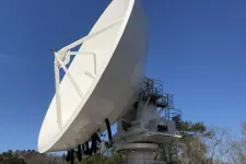 Thumbnail for Large white satellite dish antenna against clear blue sky with trees in the background