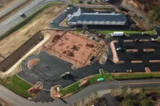 Thumbnail for Aerial view of a construction site with paved parking areas and a building near a highway intersection.