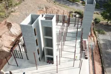 Thumbnail for Aerial view of gray concrete building under construction with exposed steel beams and workers onsite.
