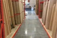 Thumbnail for Aisle in a hardware store with stacks of wooden boards organized on red metal racks on both sides.