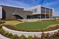 Thumbnail for Modern building with large windows adjacent to a landscaped putting green surrounded by flower beds under blue sky