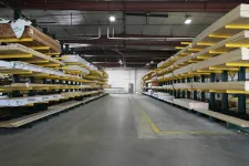 Thumbnail for Interior view of a warehouse aisle with stacked lumber on metal racks and a concrete floor under overhead lighting.