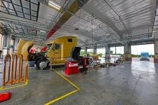Thumbnail for Interior of a large truck maintenance garage with a yellow semi truck being serviced under bright lighting.