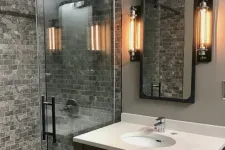 Thumbnail for Modern bathroom with glass shower, gray stone tiles, white countertop, and industrial wall light fixtures.