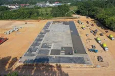 Thumbnail for Aerial view of concrete foundation construction with trucks and workers on a cleared dirt site near trees.