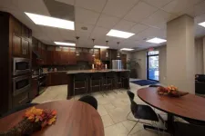 Thumbnail for Modern kitchen and dining area with dark wood cabinetry, island seating, and round tables with floral centerpieces.