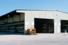 Thumbnail for Large metal warehouse with open bays storing lumber and wood products under clear blue sky.