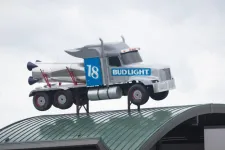 Thumbnail for Silver Bud Light truck with rocket detail mounted on a curved green rooftop against a gray sky.